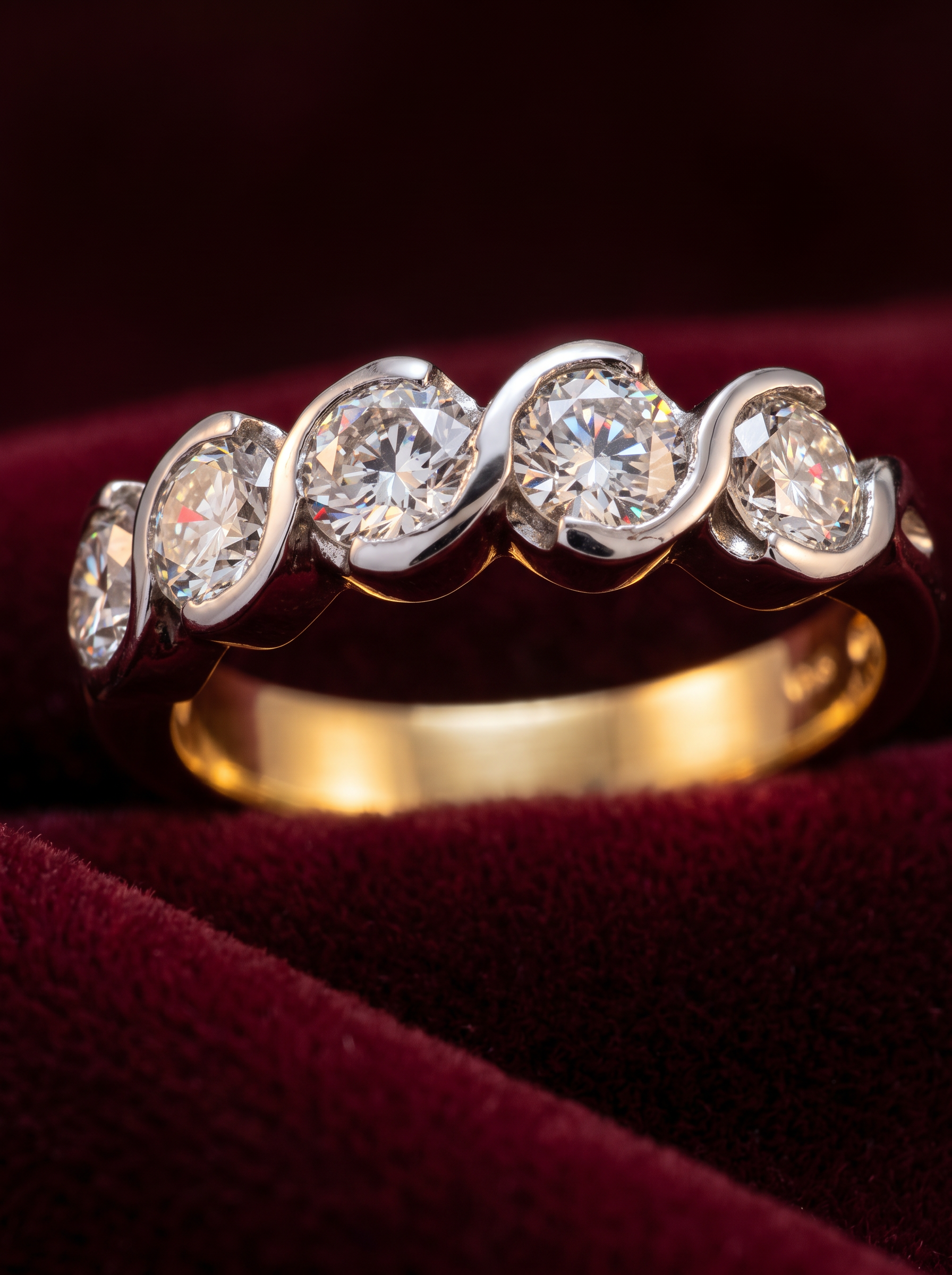 A gold and white-gold swirl diamond eternity ring made by Pedro at Glow Jewellers, resting on deep burgundy velvet